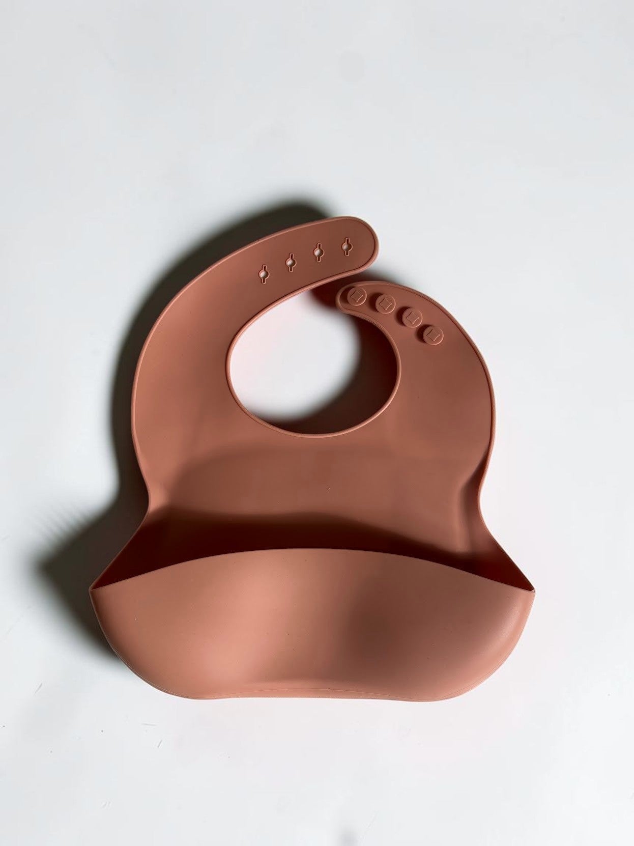 Babero de silicona Vamos Niños color terracota con bolsillo recoge-migas ajustable y libre de BPA para bebés.