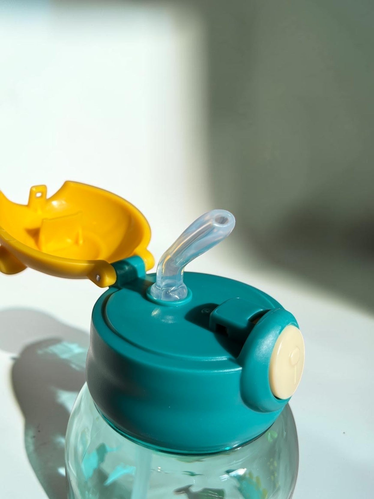 Botella de agua infantil Vamos Niños con diseño de dinosaurios, tapa azul y amarilla con pajita y botón de apertura.