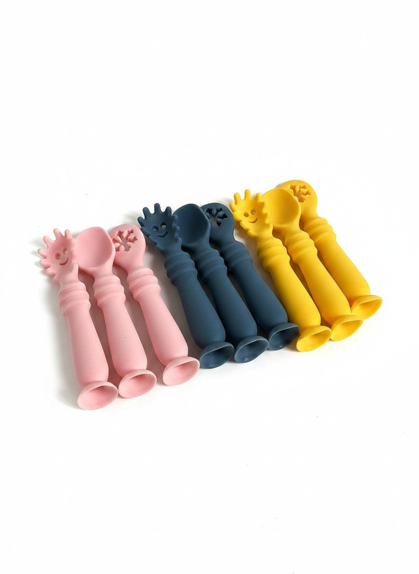 Set de cubiertos de silicona Vamos Niños en rosa, azul y amarillo con diseño ergonómico para bebés.