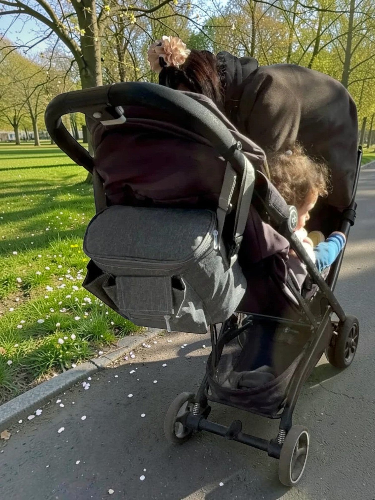 Organizador de carrito de bebé gris Vamos Niños con múltiples compartimentos, instalado en un cochecito en la calle.
