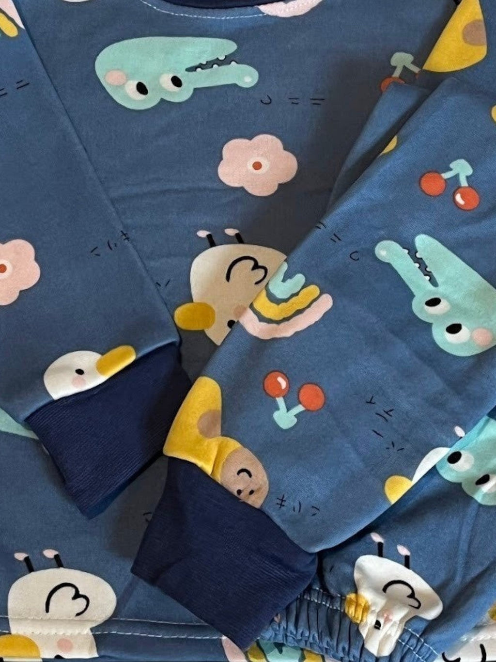 Pijama afranelado Vamos Niños azul con estampado de animalitos, flores y cerezas, con puños elásticos en las mangas.