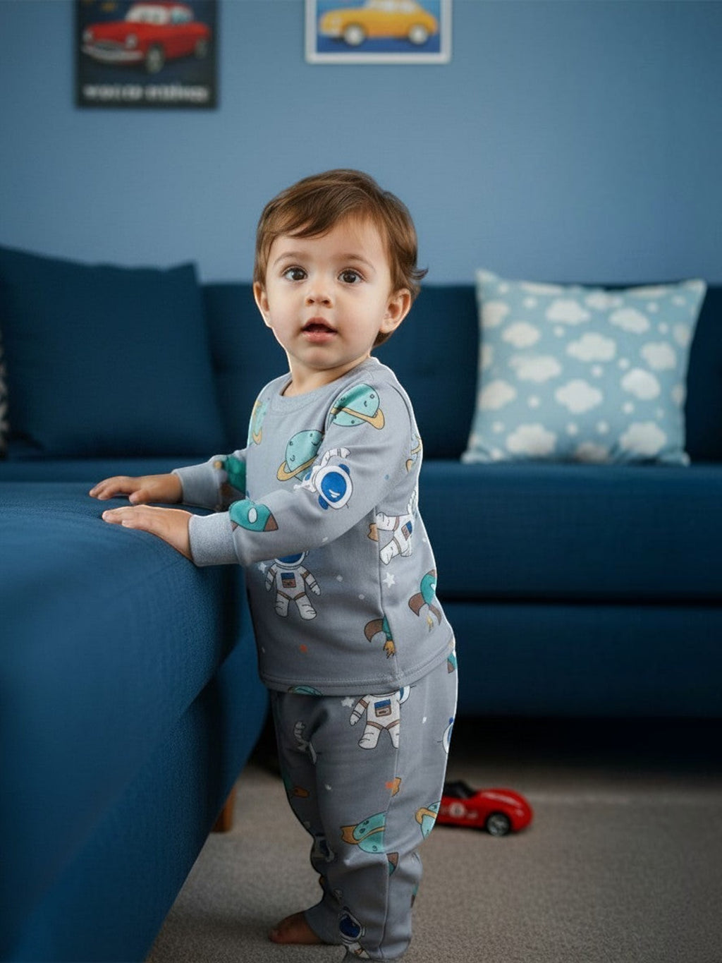 Niño pequeño vistiendo pijama afranelado gris de Vamos Niños con estampado de astronautas y planetas en una sala