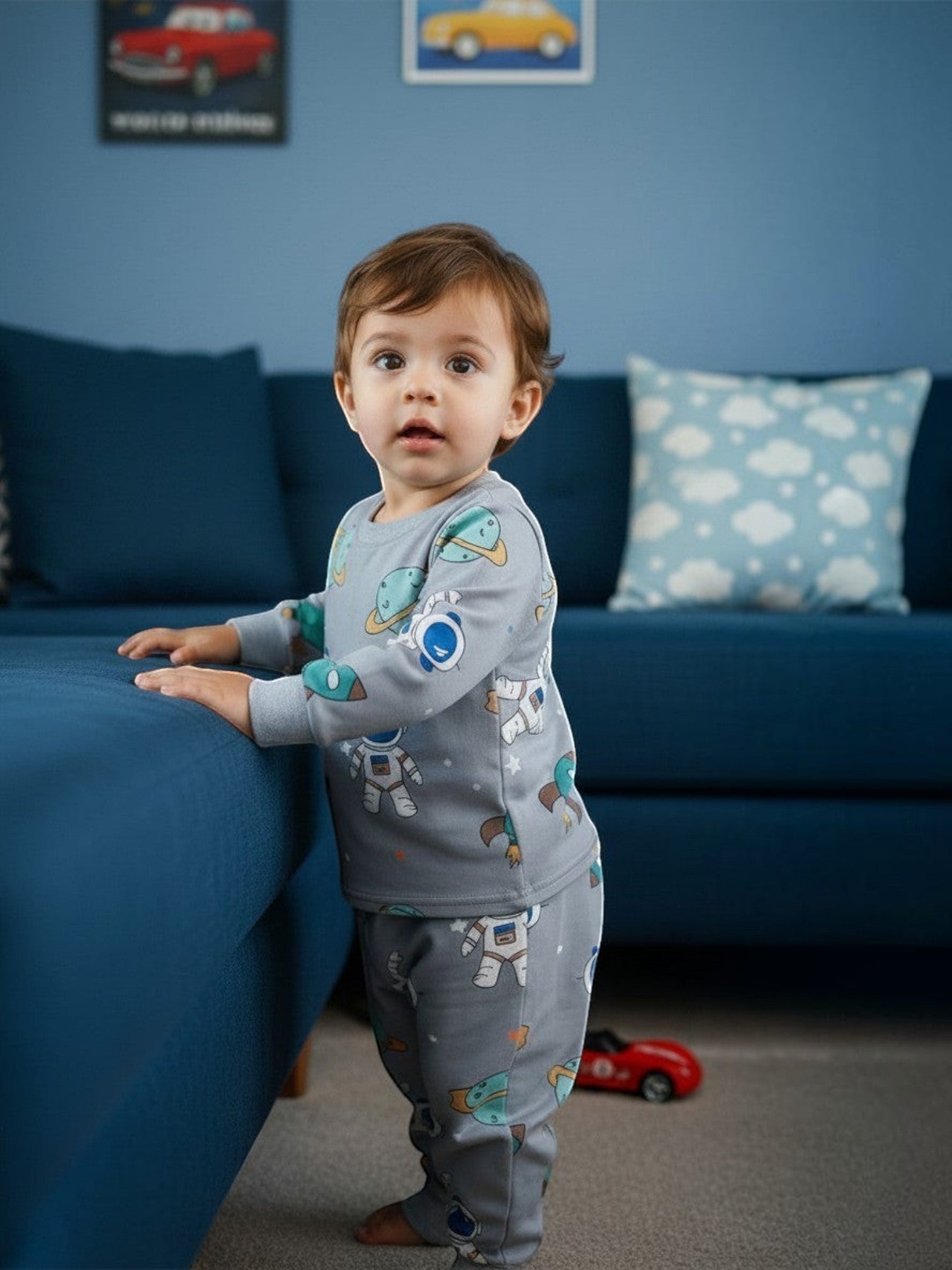 Niño pequeño vistiendo pijama afranelado gris de Vamos Niños con estampado de astronautas y planetas en una sala