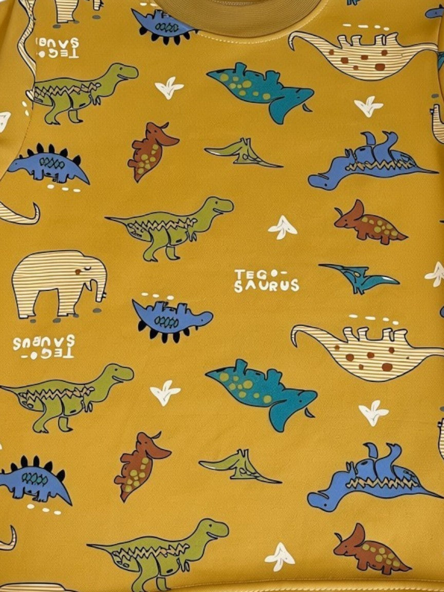 Pijama infantil Vamos Niños color mostaza con estampado de dinosaurios coloridos, manga larga y cuello redondo suave.