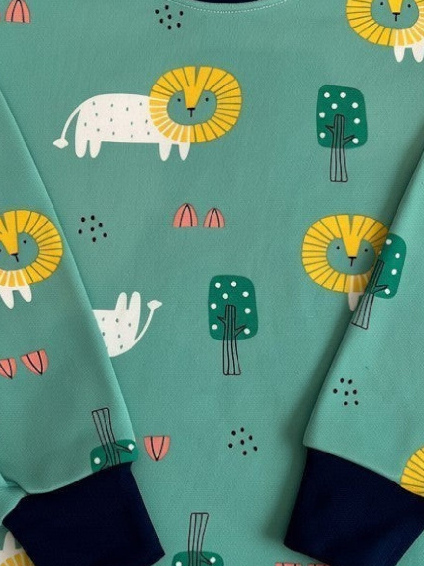 Pijama de niño Vamos Niños verde con estampado de leones y árboles, cuello y puños azul marino.