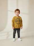 Niño pequeño vistiendo polerón amarillo de Vamos Niños con estampado de letras y dinosaurio, estilo casual.