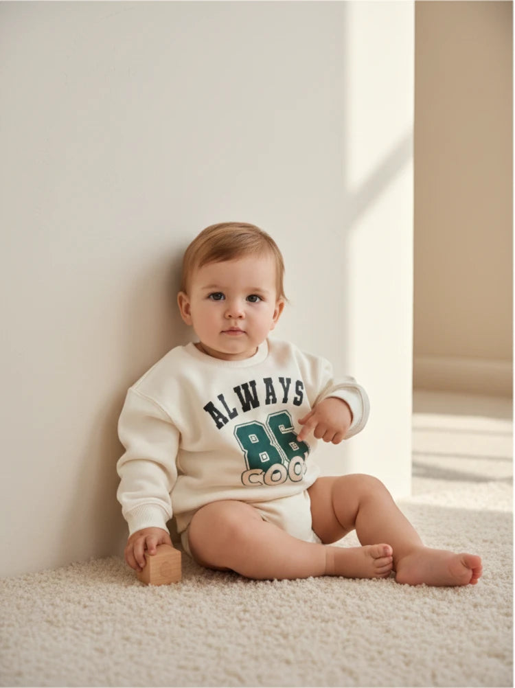 Bebé sentado usando polerón beige Lefties de Vamos Niños con estampado universitario verde en el pecho