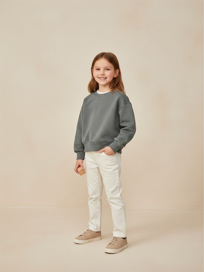 Niña sonriente vistiendo polerón gris verdoso de Vamos Niños con pantalones claros y zapatillas casuales