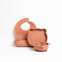 Set de alimentación Vamos Niños de silicona color terracota con babero, plato y cuenco con forma de osito para bebé.