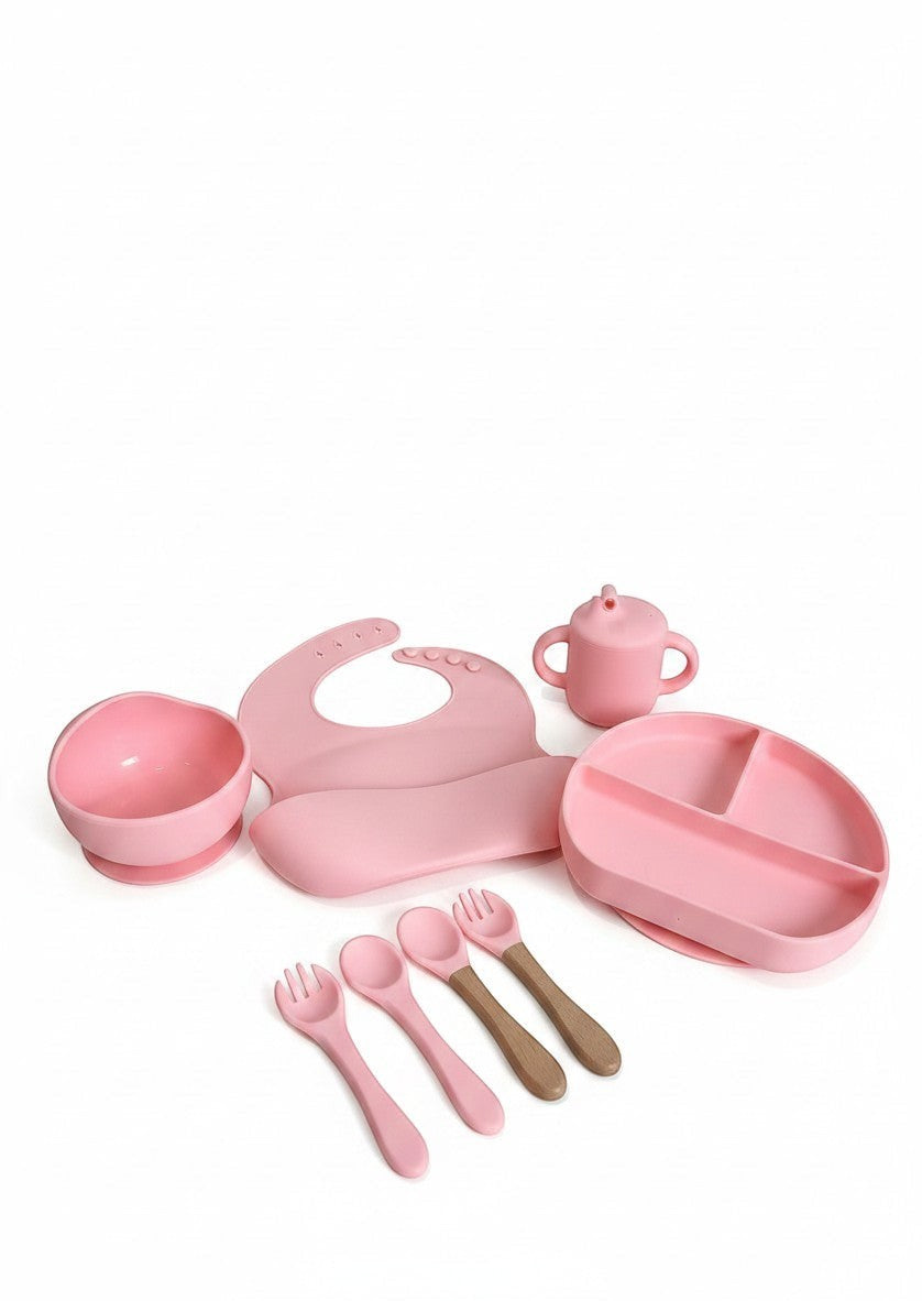 Set de alimentación Vamos Niños rosa en silicona con plato, cuenco, babero, vaso y cubiertos con mango de madera.