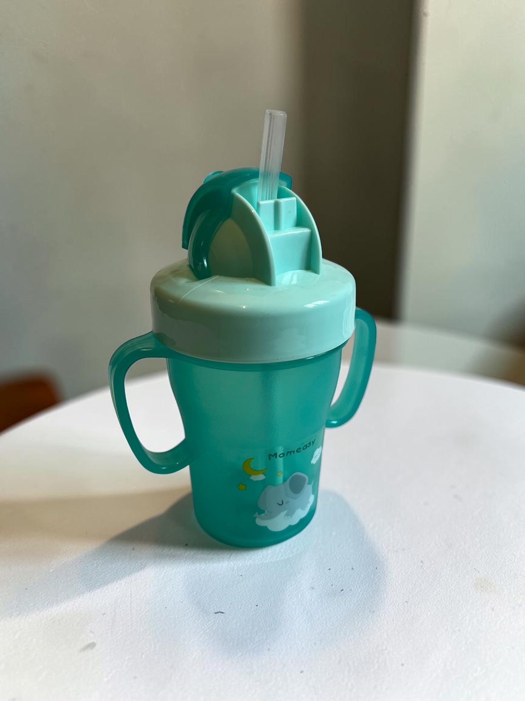 Vaso de aprendizaje verde de Vamos Niños con asas, tapa abatible y pajita de silicona. Diseño de elefante y luna.